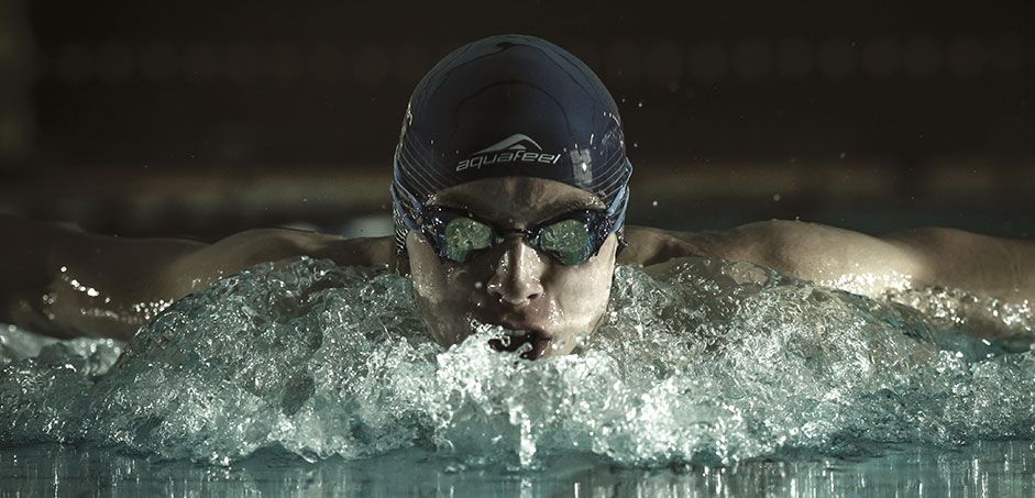 Ein Schwimmer, der aus dem Wasser auftaucht und Schwimmbrille und Schwimmmütze trägt