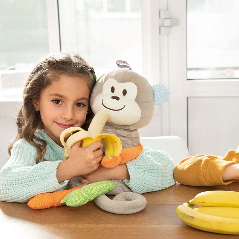 Mädchen mit einer Banane in der Hand und Affen-Plüschwärmekissen