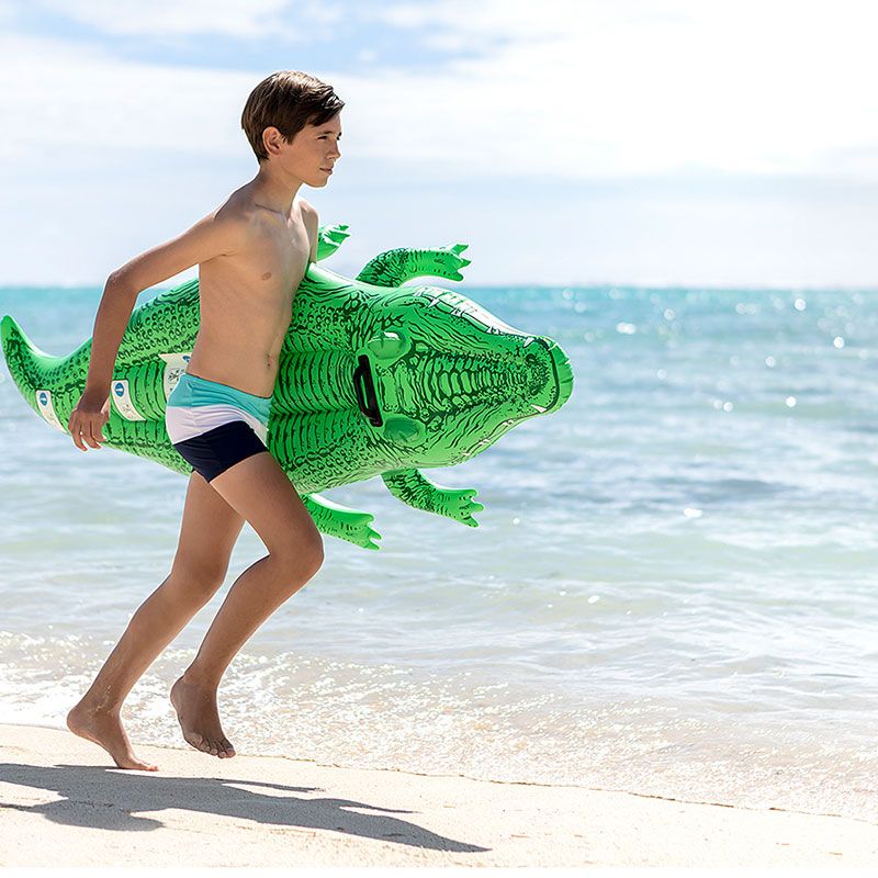Ein Junge läuft mit einem aufblasbaren Krokodil am Strand